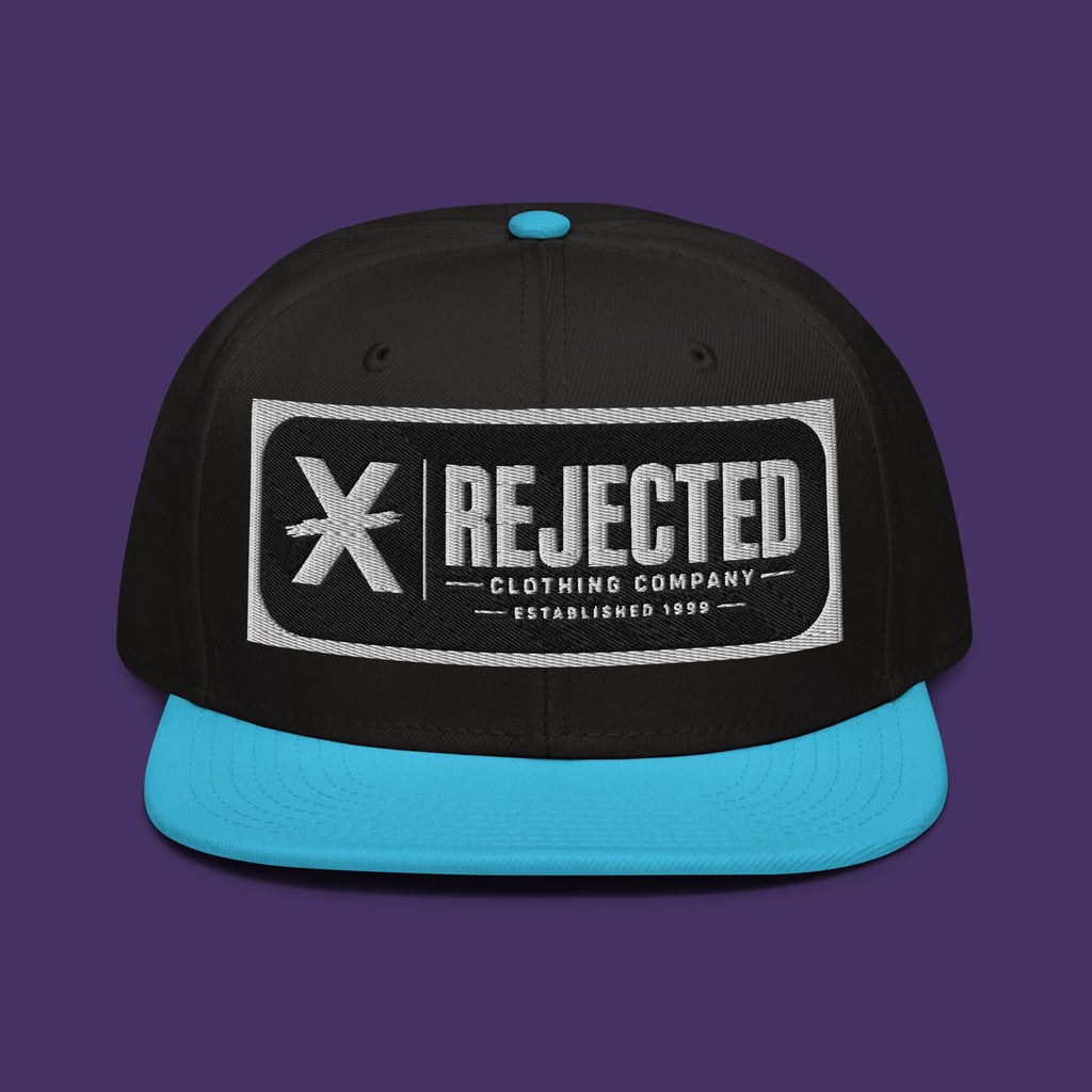 Black snapback with a teal brim and an embroidered Rejected Clothing Company Established 1999 patch