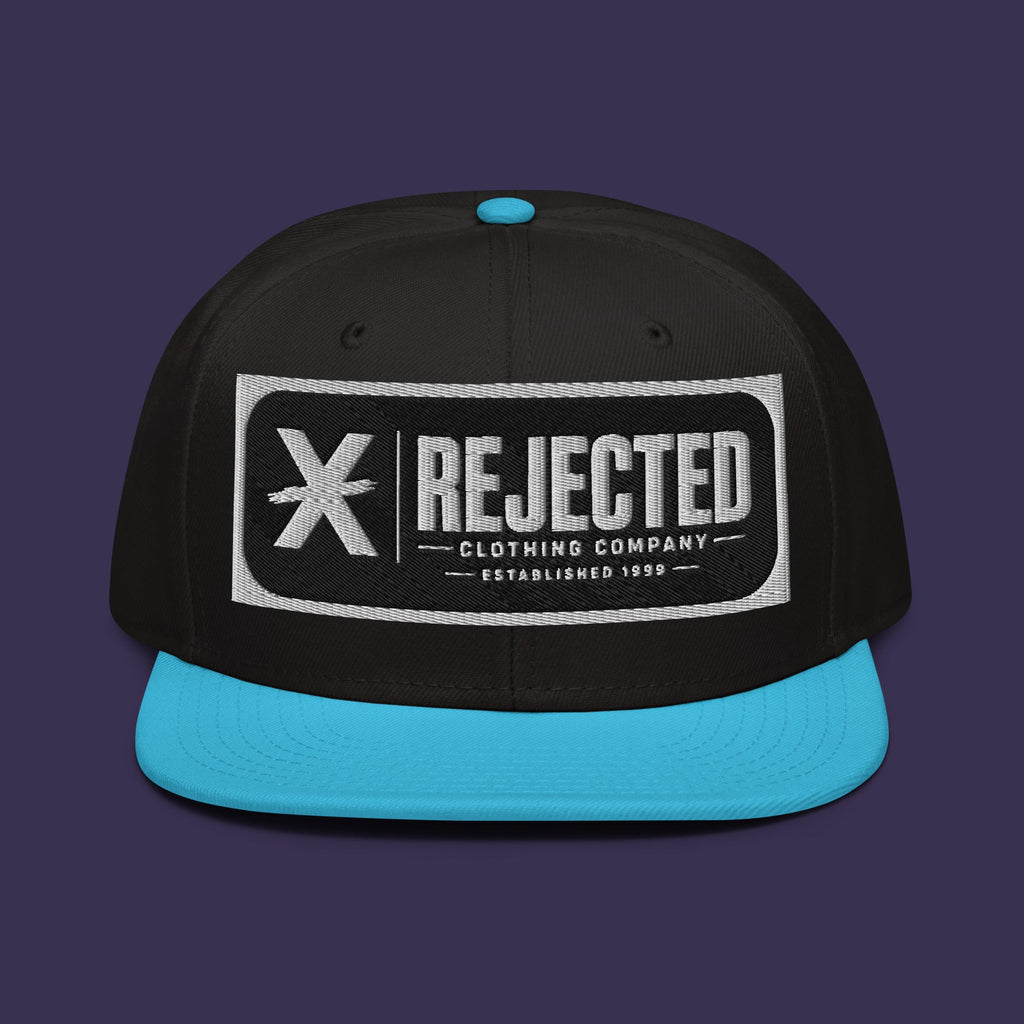 Black snapback with a teal brim and an embroidered Rejected Clothing Company Established 1999 patch
